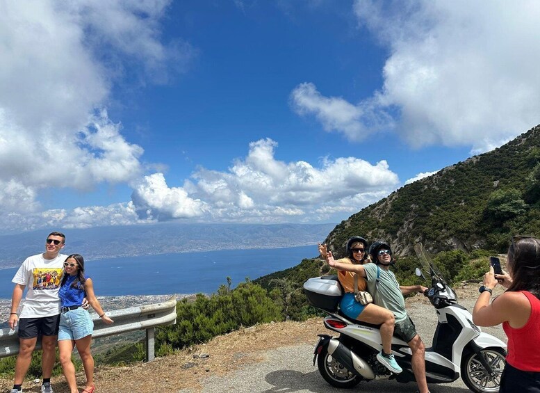 A group of people on a coastal road with a scenic view of the sea and hills. 1