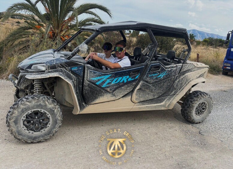 A rugged off-road vehicle with a distinctive blue and black design, parked on a dirt road with a mountainous backdrop. 3