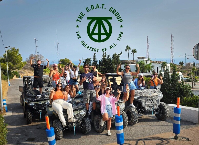 A group of people posing with ATVs in a parking lot with a coastal background. 1