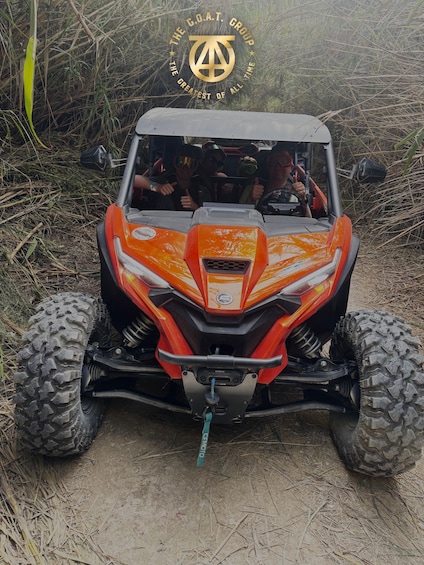 A red off-road vehicle with a logo on the windshield, parked on a dirt path surrounded by vegetation. 1