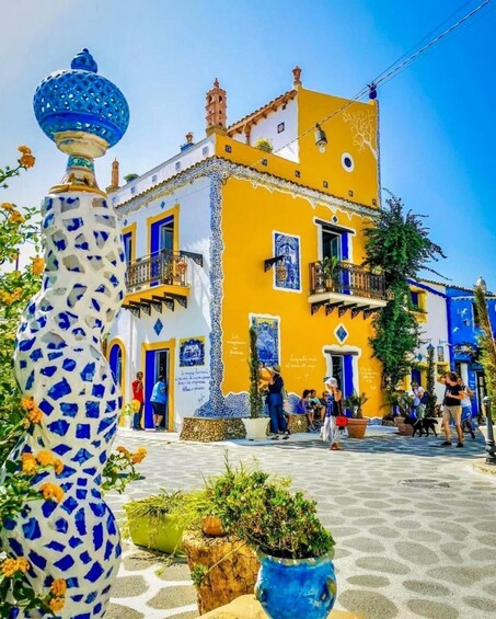 A vibrant yellow building with blue accents, a mosaic vase, and potted plants in a sunny plaza. 1