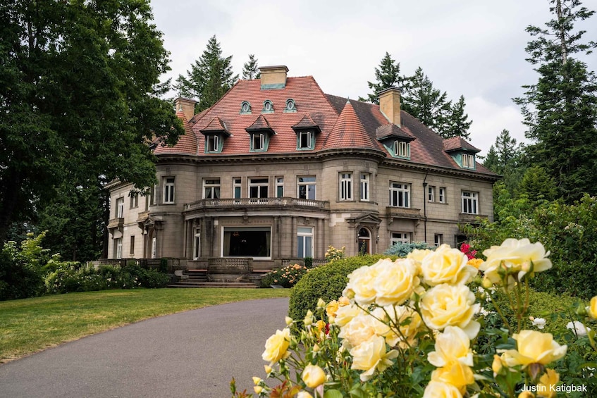 A large, historic building with a red-tiled roof, surrounded by lush greenery and blooming yellow roses. 5
