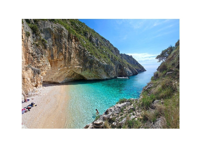 A coastal landscape with a clear turquoise sea, rocky cliffs, and a sandy beach. 4