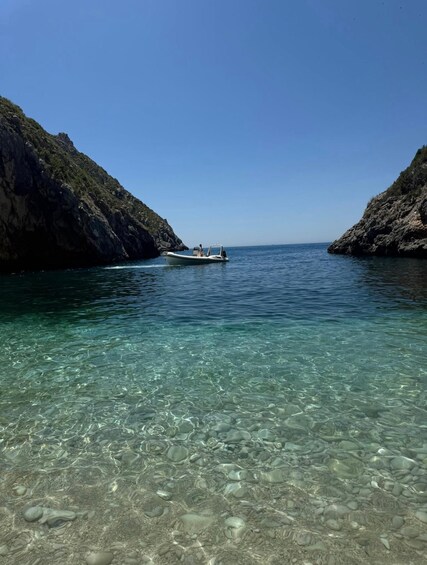 A boat on clear turquoise water with rocky cliffs on either side. 5