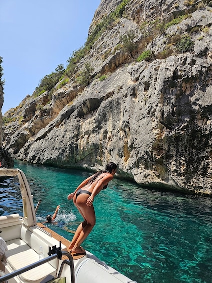 A woman in a bikini diving into clear blue water from a boat, surrounded by rocky cliffs. 2