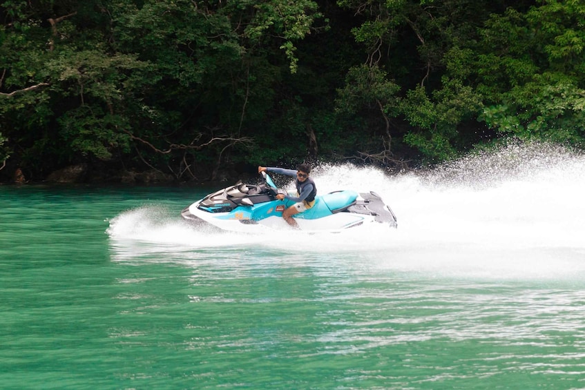 A person jet-skiing on turquoise water surrounded by dense green foliage. 5