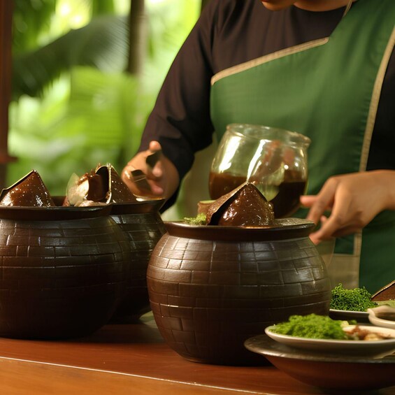 A person in a green apron preparing food in large ceramic pots. 2