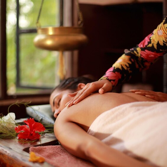 A person receiving a massage with a decorative lamp and flowers in the background. 1