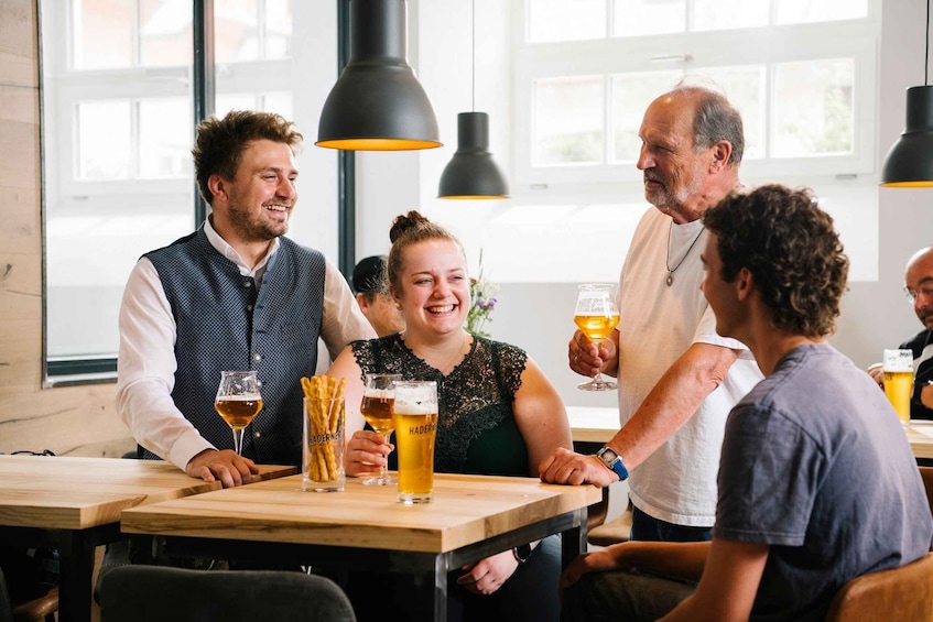 A group of people sitting at a wooden table in a restaurant with hanging pendant lights. 1