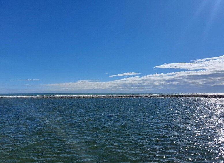 A calm sea with gentle waves, a clear blue sky, and a distant shoreline. 1