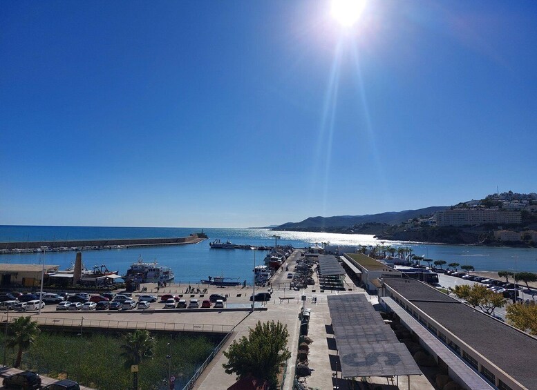 A coastal marina with boats, a parking lot, and a hillside with buildings. 2