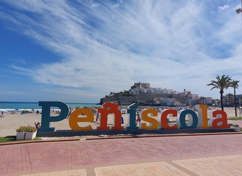 A beach with a large sign reading 'Peníscola' and a castle in the background. 3