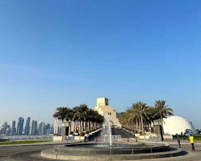 A fountain, palm trees, a dome-shaped building, and a city skyline in the background. 2