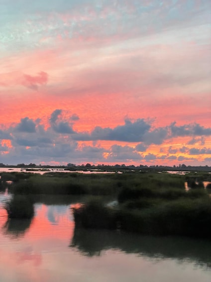 A sunset over a marshy landscape with water reflecting the sky. 1