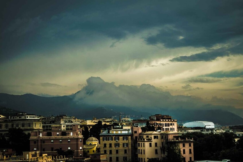 A cityscape with historic buildings and a dome-shaped structure, likely a stadium, under a cloudy sky with mountains in the background. 2