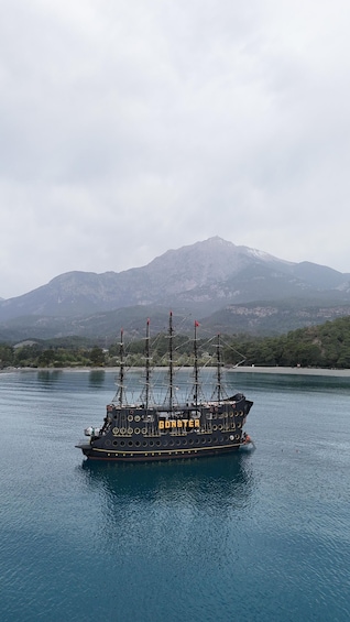A ship named 'GONSTER' on calm waters with a mountainous backdrop. 1