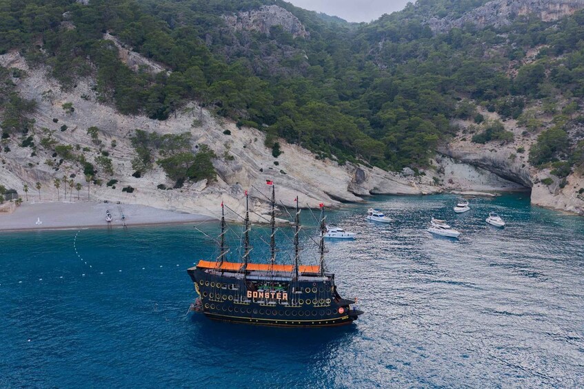 A ship named 'GONSTER' sailing in a coastal area with rocky cliffs and a beach. 1