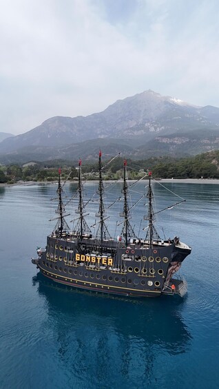 A tall ship named 'GONSTER' sailing on calm waters with a mountainous backdrop. 4