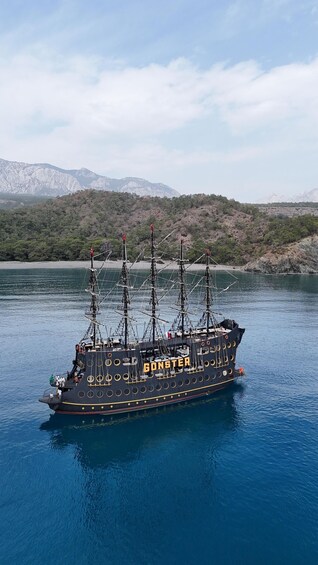 A tall ship named 'GONSTER' sailing on a calm body of water with mountains in the background. 5
