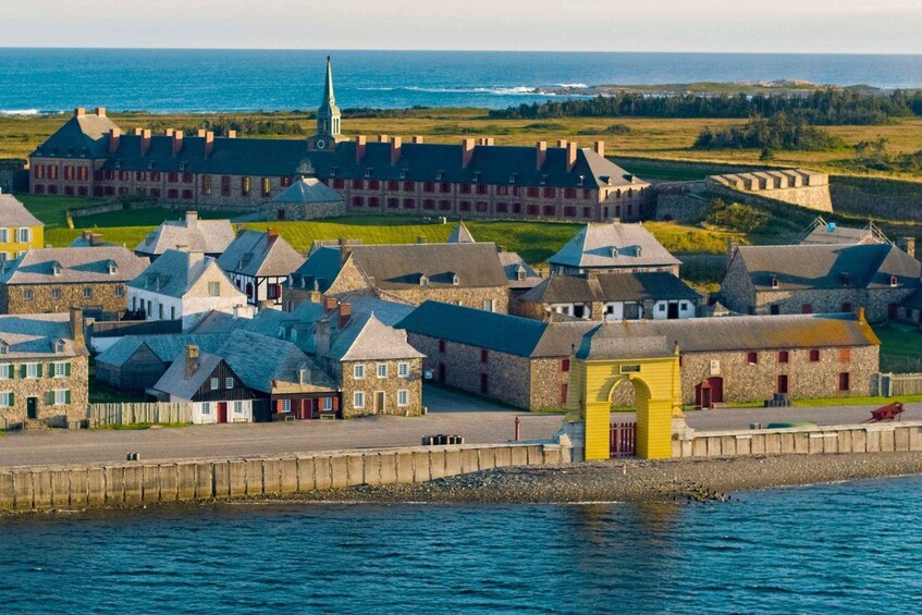A coastal town with historic stone buildings, a prominent yellow building, and a church steeple. 1