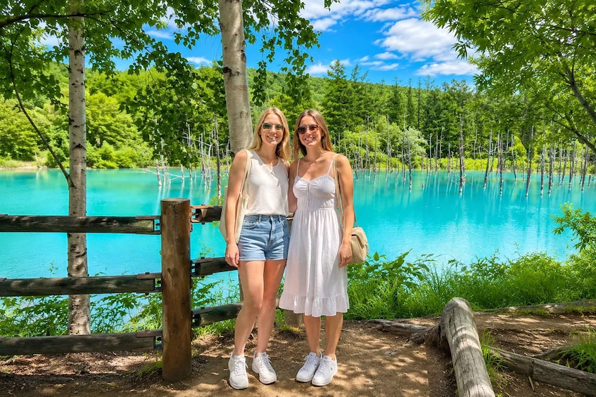 Two people standing by a turquoise lake surrounded by greenery. 4