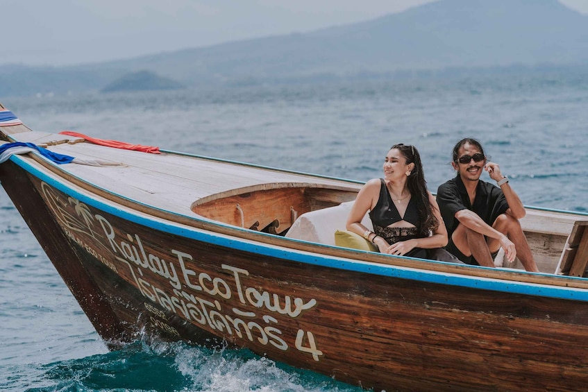 Two people on a wooden boat with 'Railay Eco Tour' written on it, sailing on the water. 1