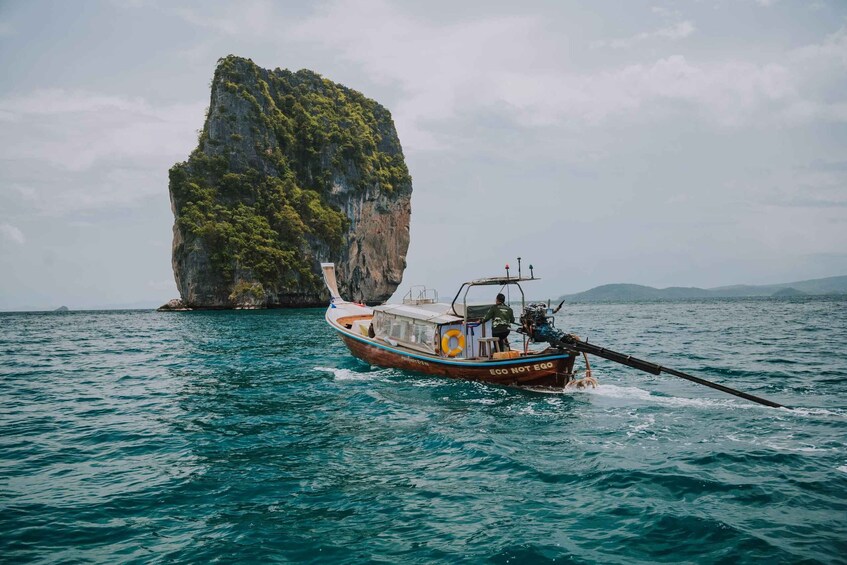 A boat with 'ECO NOT EGO' written on its side, anchored near a large rock formation surrounded by water. 4