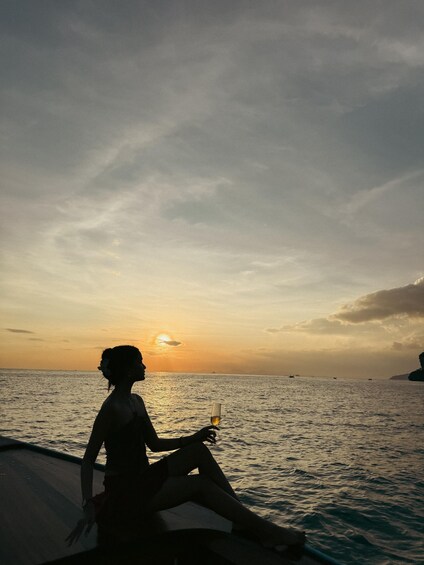 A person sitting on a boat during sunset, holding a drink. 5