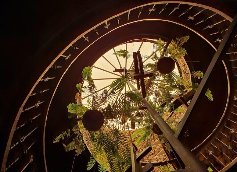 A spiral staircase with a circular window, surrounded by ferns and a wooden cross. 5