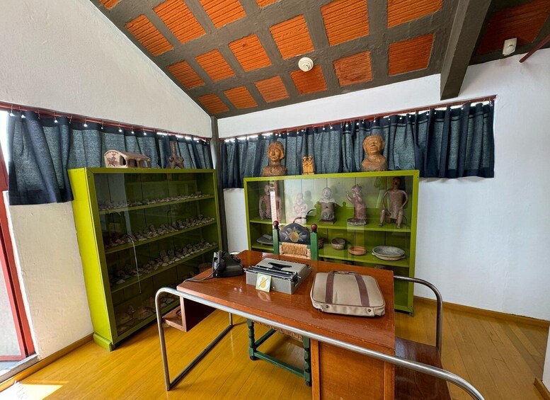A room with wooden flooring, a desk with a bag, and shelves with figurines and pottery. 5