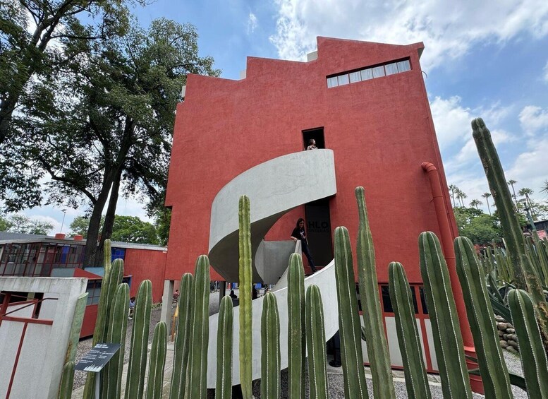 A red building with a unique curved white structure, surrounded by cacti. 5