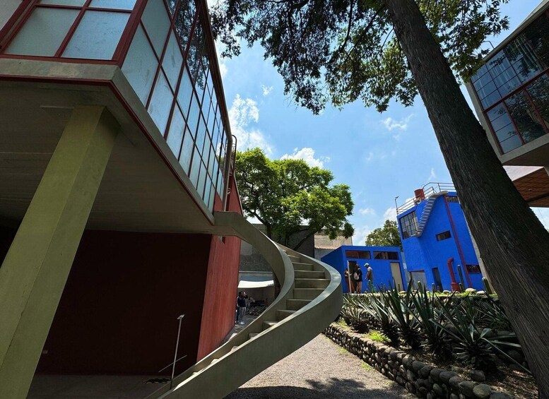 A modern building with a spiral staircase, a blue structure, and a tree in the foreground. 1