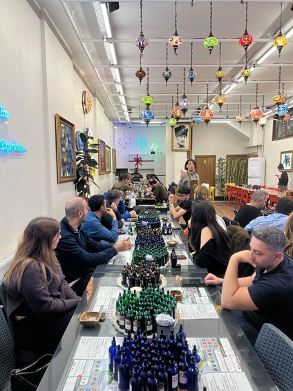 A group of people seated at a long table with various bottles in front of them, in a room with hanging decorative lights. 3