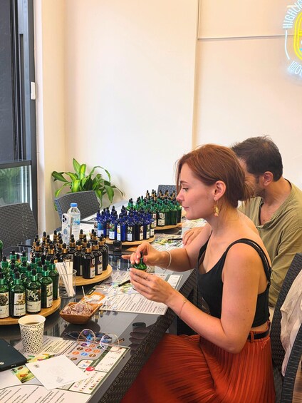 A woman examining a small bottle at a table with various bottles and papers. 2