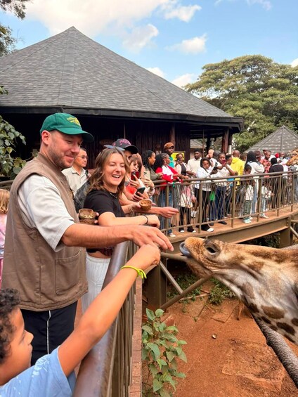 Eine Giraffe in einer Zooanlage, während Besucher sie füttern. 1