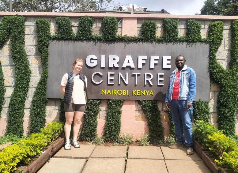 Schild für das Giraffen-Zentrum in Nairobi, Kenia, mit viel Grün und einem gepflasterten Weg. 2