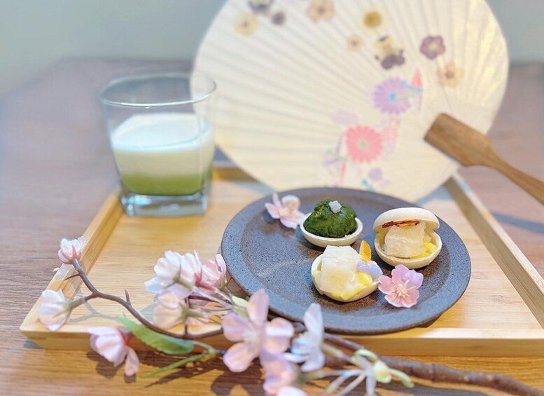 A traditional Japanese tea set with a green tea, a small dish of matcha, and two mochi desserts on a wooden tray. 1