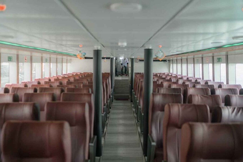A train interior with rows of brown leather seats, a central aisle, and overhead luggage compartments. 1