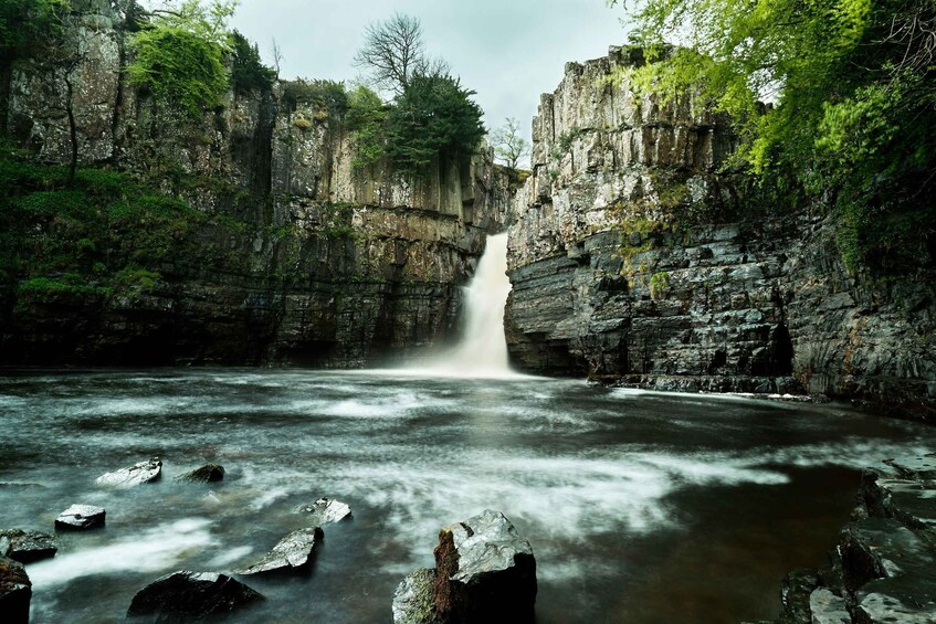 A waterfall cascading into a river surrounded by rocky cliffs and dense greenery. 1