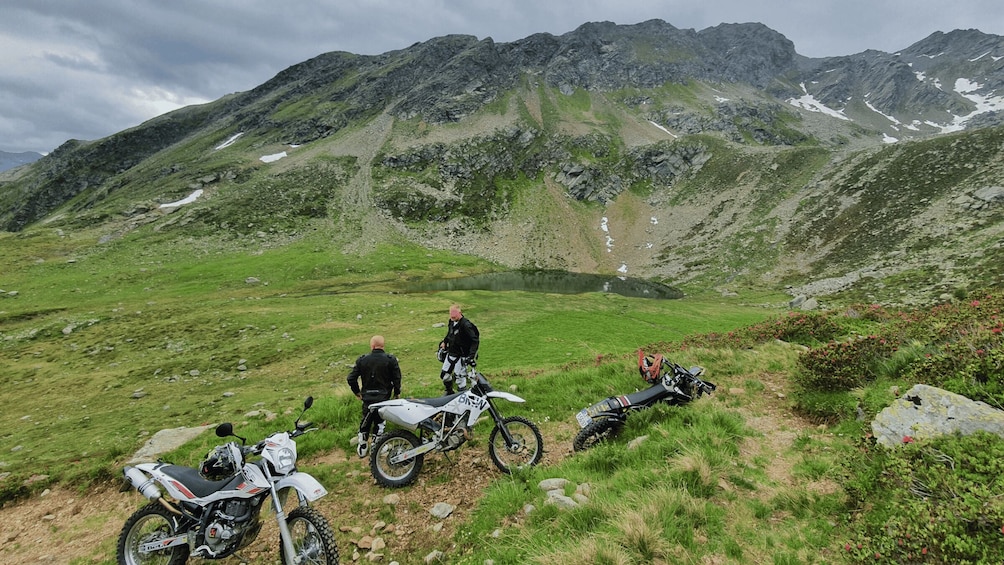 A mountainous landscape with two dirt bikes parked on a grassy path. 2