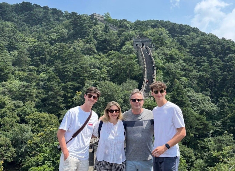 A group of people standing in front of the Great Wall of China, surrounded by lush greenery. 4