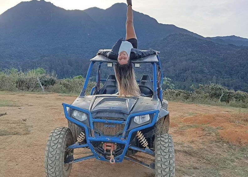 A person performing a handstand on a blue off-road vehicle with a mountainous landscape in the background. 2