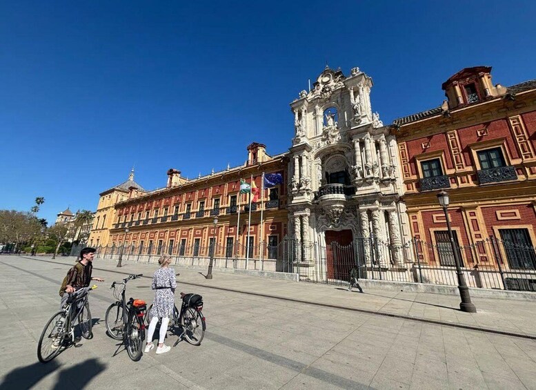 A historic building with ornate architecture, a clear blue sky, and a paved plaza with bicycles. 1