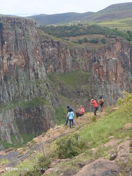 A group of people hiking on a rocky terrain with a deep valley and distant hills. 5