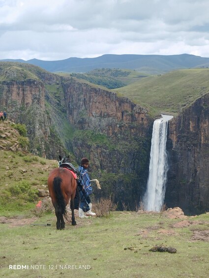 A person on horseback overlooking a waterfall in a mountainous landscape. 3