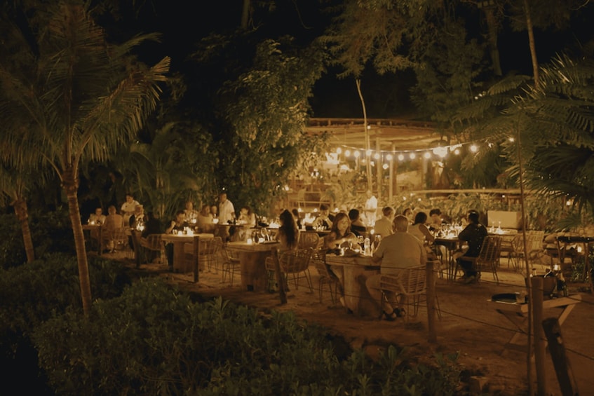 An outdoor dining area with tables and chairs, surrounded by greenery and palm trees. 4