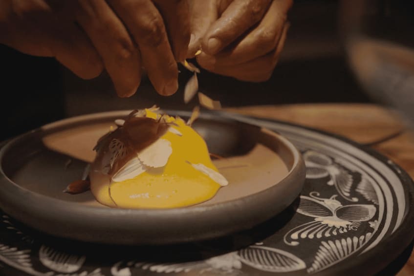 A person peeling a fruit, possibly a mango, over a bowl. 2