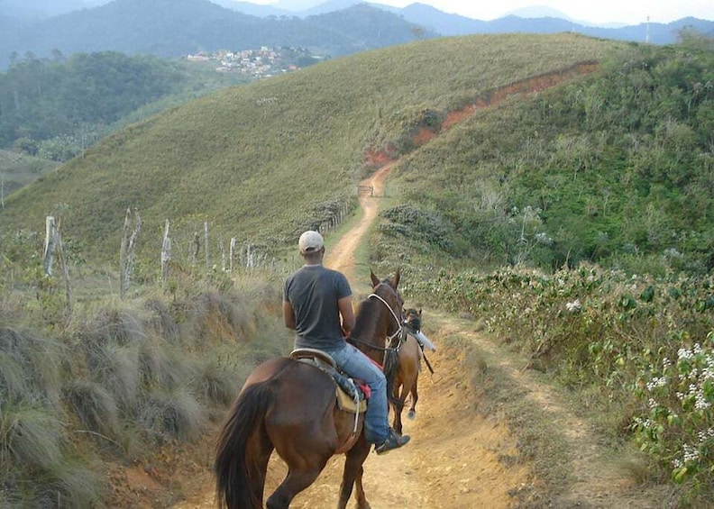 Two people riding horses on a dirt path through a hilly landscape. 5