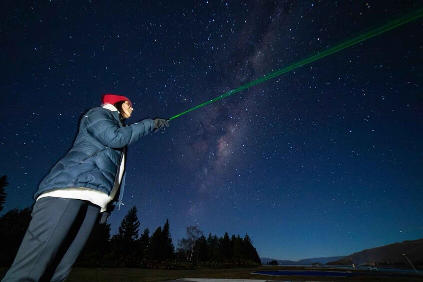 A person holding a green laser pointer against a starry night sky. 5