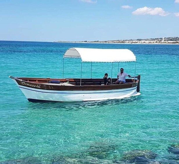 A boat named 'Buccaneer' on clear turquoise water with a white canopy, two people on board, and a coastline in the background. 5